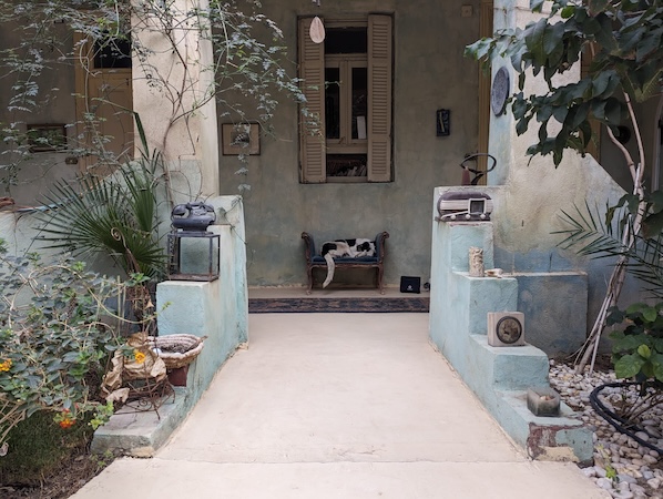A cozy entrance to a rustic home with a cat lounging on the porch, surrounded by potted plants and decorative pottery.